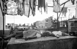 Two children laying on their backs underneath a clothes line, looking up at the sky.